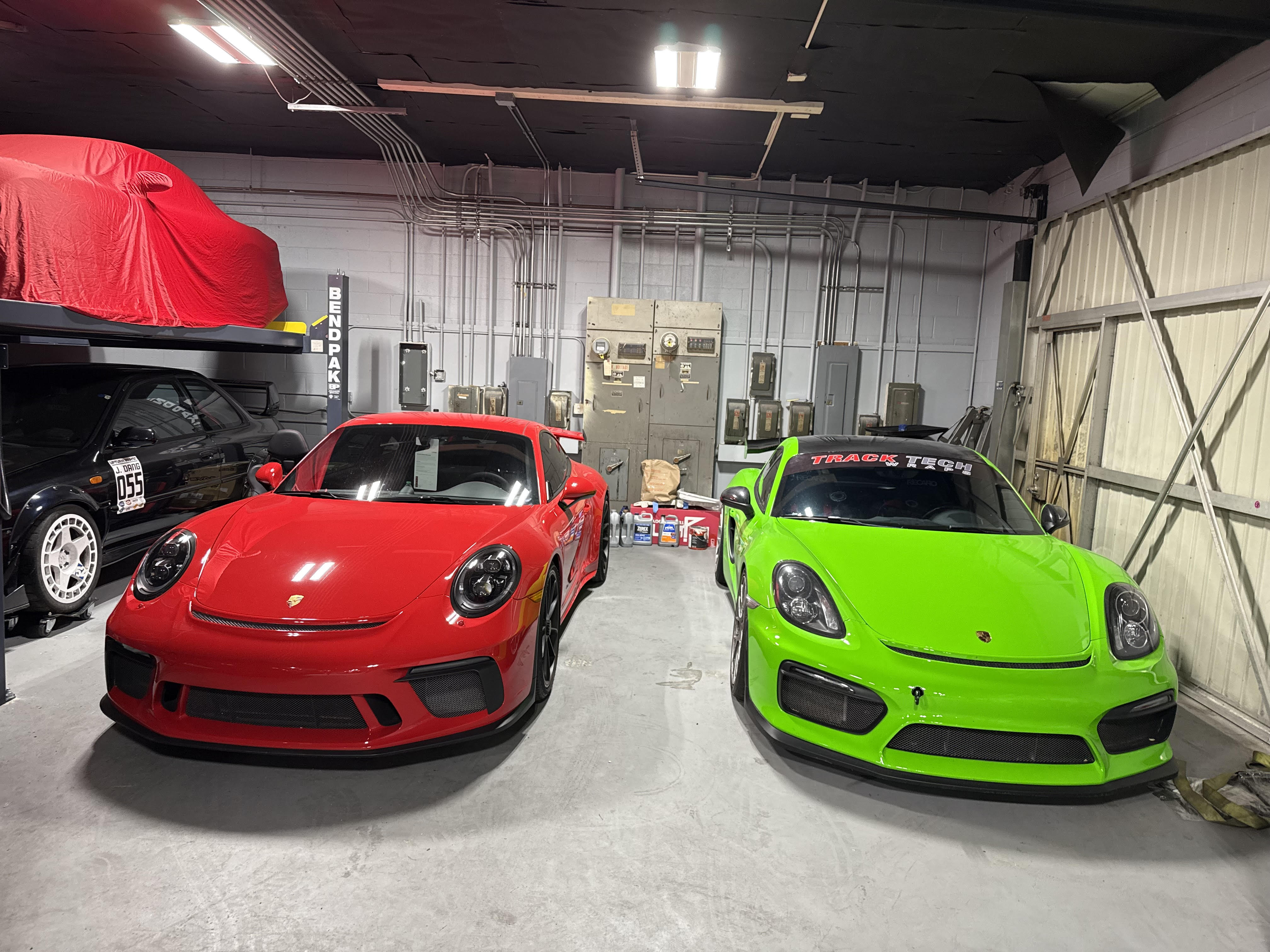 Red Porsche GT3 and green Cayman GT4 in the Track Tech shop